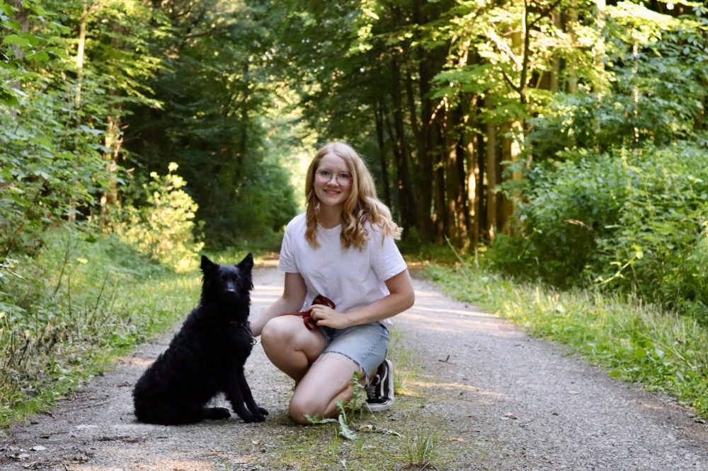 Klara Ortmann lächelt, neben ihr sitzt Pippa auf einem Waldweg