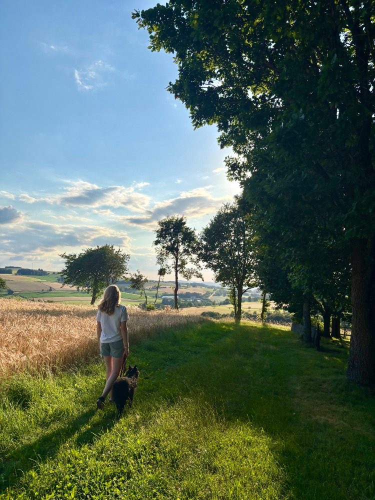 Klara spaziert mit Pippa an einem Kornfeld entlang, Blick über die Rhön